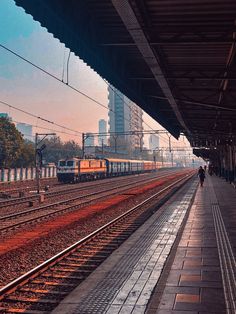 a train station with two trains on the tracks and people walking near by at sunset