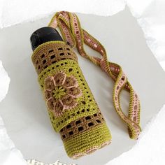 a crocheted water bottle cover with a flower on it and a lanyard around the neck