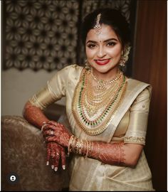 a woman in a white sari and gold jewelry poses for the camera with her hands on her chest