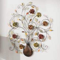 a decorative metal wall sculpture with flowers and leaves on it's sides, hanging from a white wall