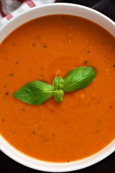 a white bowl filled with tomato soup and garnished with green leafy basil