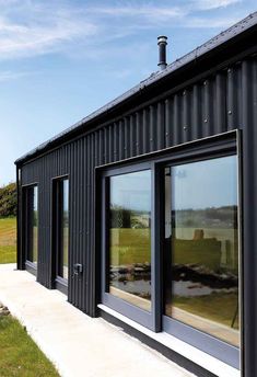 the side of a black building with large windows on it's sides and grass in front