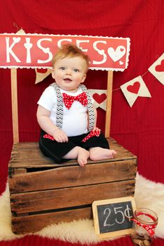 a baby sitting on top of a wooden crate in front of a sign that says kiss kisses