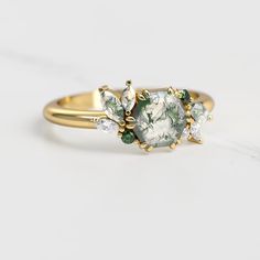 a close up of a ring on a white surface with green and white stones in the middle