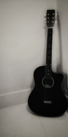 an acoustic guitar leaning against the wall in a room with white walls and flooring