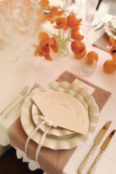 a table set with plates, silverware and orange flowers in vases on the table