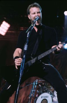 a man holding a guitar while standing in front of a microphone on top of a stage