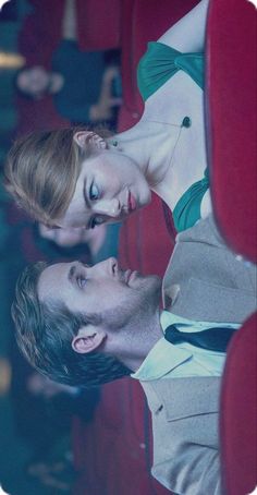 a man and woman sitting next to each other on a red chair in an auditorium