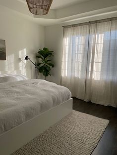 a white bed sitting next to a window in a bedroom under a light fixture on top of a wooden floor