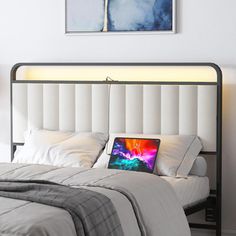 a bed with a laptop on it in a white room next to a painting and lamp