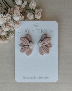 the clay and fern co earrings are on display next to some dried flowers, which have been placed in front of a white card