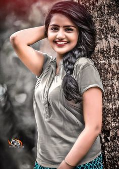 a woman standing next to a tree with her hand on her head and smiling at the camera