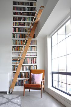 there is a ladder in the corner of this room with bookshelves and a chair