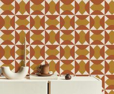 an orange and white geometric wallpaper with a teapot on the cabinet next to it