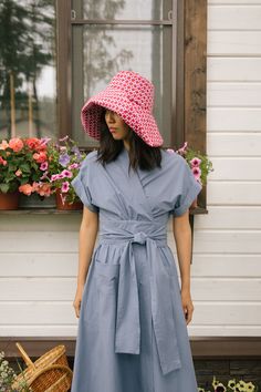 a woman standing in front of a window wearing a blue dress and pink polka dot hat