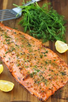 a piece of salmon on a cutting board with lemons and parsley next to it