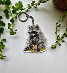 a raccoon keychain is hanging on a wall next to some plants