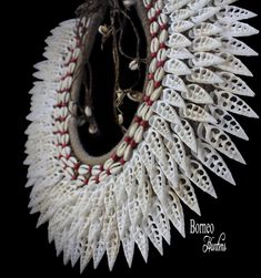 A Papua New Guinea traditional tribal handmade light brown braided rope large curved necklace, decorated with three overlapping bands of long pointed sliced white Shells. The inner band of the necklace is decorated two lines of cream Cowrie Shells and red painted round Wood beads. The sliced pointed Shells are between 1.5 inches, and 1.9 inches in drop length. The inner width of the necklace is 5.25 inches, and the outer width is 15.5 inches. The necklace has a drop length of 14 inches, and is f Traditional Shell Jewelry For Festival, Traditional Handmade Shell Necklace For Festival, Traditional Shell Necklace For Beach, Traditional Handmade Shell Necklaces, Traditional Handmade Shell Necklace, Traditional Multi-strand Beach Jewelry, Red Braided Bohemian Jewelry, White Bohemian Ceremonial Necklace, White Shells