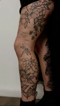 a woman's legs with flowers and leaves tattooed on her leg, while wearing black boots