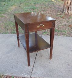 a small wooden table sitting on top of a cement ground next to a tree and grass