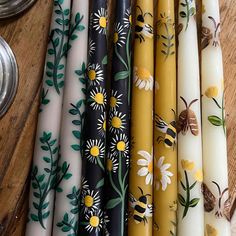 several different colored candles are lined up on a wooden table with bees and flowers painted on them