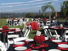 tables set up with black and red linens for an outdoor wedding reception in the grass