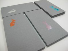 four business cards with different colored designs on the front and back cover, all in grey paper