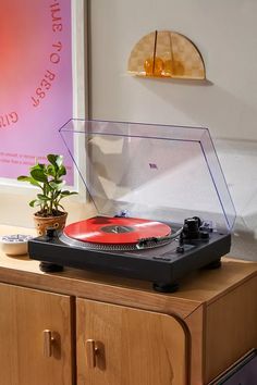 a record player sitting on top of a wooden cabinet next to a potted plant