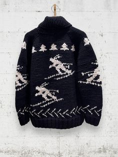 This authentic Cowichan sweater was knit by indigenous makers in Vancouver Island and the mainland of British Columbia. Each sweater is inspired from the original 19th century designs hand-knit by the Cowichan, a Coast Salish people in British Columbia. Authentic Cowichan sweaters are so distinctive and prized that in 2011, the Canadian government recognized Cowichan knitters and sweaters as nationally and historically significant. Our exclusive design incorporates miniature skiers into a black Black Wool Hand Knitted Sweater, Black Nordic Jacquard Knit Sweater, Black Wool Sweater With Fair Isle Pattern, Traditional Winter Knitted Sweater, Nordic Wool Sweater Hand Knitted, Nordic Wool Knit Sweater, Nordic Hand Knitted Wool Sweater, Nordic Black Sweater With Fair Isle Pattern, Nordic Style Hand Knitted Wool Sweater