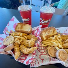 two sandwiches and french fries are sitting on a table next to cups of sodas