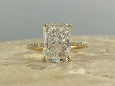 a large diamond ring sitting on top of a stone slab with diamonds surrounding it and the band in yellow gold