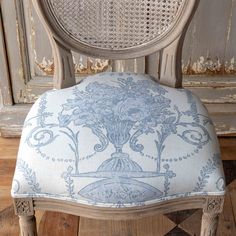 an old chair with a blue and white floral design on the back, sitting in front of a wooden door