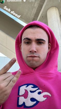 a man in a pink hoodie is making the peace sign with his fingers while standing under an overpass