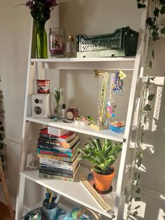 a white book shelf filled with books next to a plant and other items on top of it