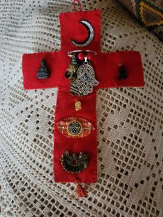 a cross made out of red fabric with buttons and charms on it sitting on a table