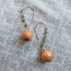 two pairs of earrings are sitting on a blue and white fabric surface, one has an orange beaded earring