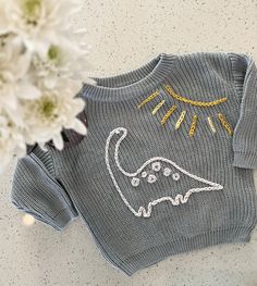 a knitted sweater with an image of a dinosaur on it next to white flowers