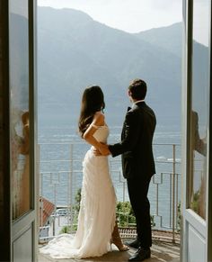 a bride and groom standing in front of an open door looking out at the water