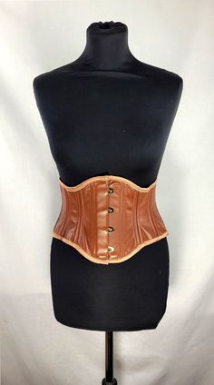 "This corset has been made from a butter soft leather in a pecan brown colour. It has a matching dark caramel silk boning casings and handmade silk binding to finish the top and bottom. Handmade, spiral steel boned corset. This waspie underbust corset is a new edition to our collection, works well if you have a shorter torso or if you only require cinch at the waist. Back laced with a matching double satin quarter inch wide ribbon. The silk is backed with woven vilene, which then has a British h Elegant Fitted Brown Corset Belt, Elegant Brown Corset, Medieval Style Brown Overbust Corset, Brown Underbust Corset, Fitted Vintage Brown Corset, Fitted Leather Underbust Corset, Brown Fitted Steampunk Corset Belt, Fitted Underbust Leather Corset, Fitted Leather Overbust Corset