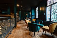 an empty restaurant with wooden floors and green walls, blue velvet chairs and tables in front of large windows