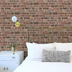 a white bed sitting next to a brick wall with two lamps on top of it