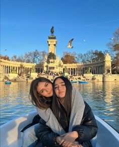 two women are sitting in a boat on the water and one is holding her arm around another woman's shoulder