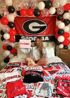 a woman sitting on top of a bed in front of a college sign and balloons