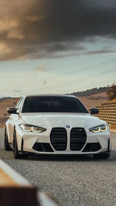 the front end of a white car driving down a road with dark clouds in the background