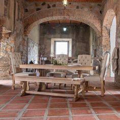 a table and chairs in a room with brick walls, stone flooring and an arched doorway