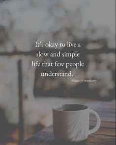 a coffee cup sitting on top of a wooden table next to a window with the words, it's okay to live a slow and simple life that few people understand