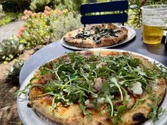 two pizzas sitting on top of white plates covered in greens next to each other