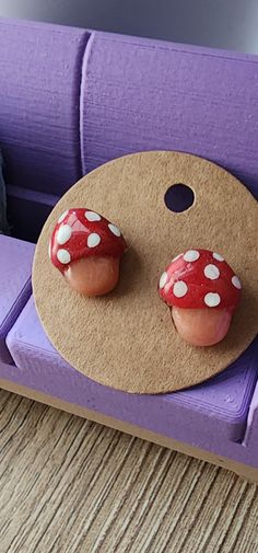 two red mushrooms sitting on top of a purple chair next to a wooden board with white polka dots