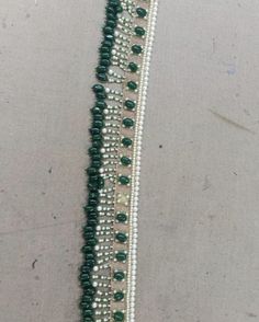 a green and white beaded bracelet with beads on the end is sitting on a table