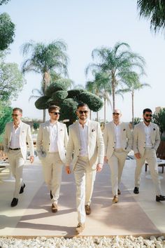 a group of men in suits and sunglasses walking down a sidewalk next to palm trees